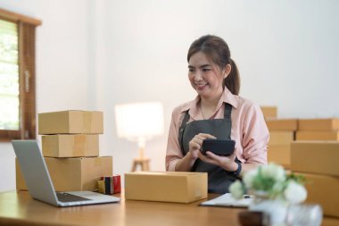 İnternetten ecommerce alışverişinde çalışan genç bir kadın. Genç bir kadın müşteriye teslim etmek için bir paket ürün satar. Çevrimiçi satış, ekommerce. Ürün çevrimiçi satılıyor.