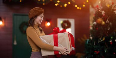 Noel Baba şapkası takan mutlu kadın hediye kutusunu tutuyor. Olumlu duygusal Noel Baba kızı. Arka planda güzel dekore edilmiş bir Noel ağacı var. Şenlikli Xmas konsepti.