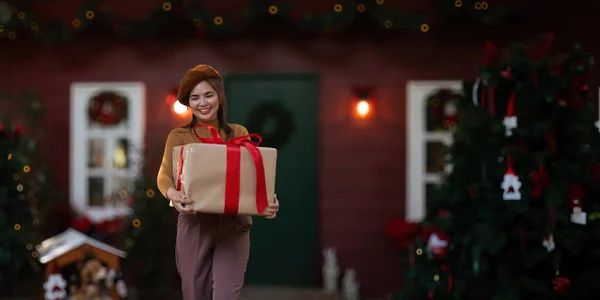 快乐的女人戴着圣诞礼帽 手里拿着礼品盒 积极的感情的圣诞老人 背景是一棵装饰精美的圣诞树 圣诞佳节的概念 — 图库照片