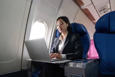 Güzel iş kadını Asyalı pencere kenarında oturmuş laptopla çalışırken kulaklıkla müzik dinliyor..