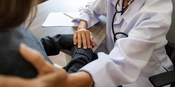 Лікар Старша Жінка Носить Білу Медичну Форму Тримаючи Руку Пацієнта — стокове фото