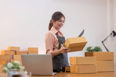 İnternetten ecommerce alışverişinde çalışan genç bir kadın. Genç bir kadın müşteriye teslim etmek için bir paket ürün satar. Çevrimiçi satış, ekommerce. Ürün çevrimiçi satılıyor.