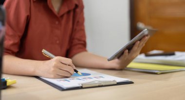 Dijital tablet finansal özet grafiği olan iş kadını ofisinde oturuyor. Ofisteki yatırım grafiğini analiz eden genç bir kadın.