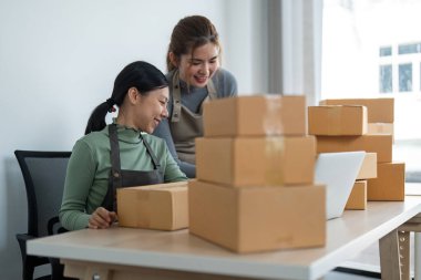 İş yerinde bilgisayarla çalışan küçük bir işletme sahibi. İki kadın satıcı ürün siparişini kontrol ediyor. Müşteriye teslimat için mal paketliyorum. Çevrimiçi satış. Ticaret için. Çevrimiçi Alışveriş.