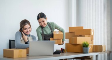 İş yerinde bilgisayarla çalışan küçük bir işletme sahibi. İki kadın çek ürün siparişi satıyor. Müşteriye teslimat için mal paketliyorum. Çevrimiçi satış. Ticaret için. Çevrimiçi Alışveriş.