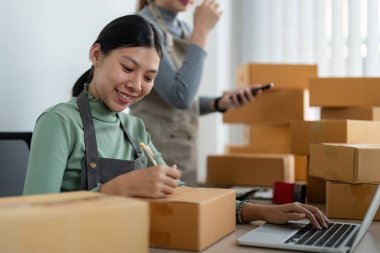 İş yerinde bilgisayarla çalışan küçük bir işletme sahibi. İki kadın satıcı ürün siparişini kontrol ediyor. Müşteriye teslimat için mal paketliyorum. Çevrimiçi satış. Ticaret için. Çevrimiçi Alışveriş.