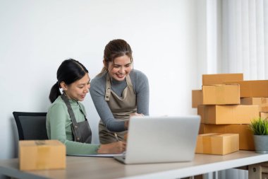 İş yerinde bilgisayarla çalışan küçük bir işletme sahibi. İki kadın çek ürün siparişi satıyor. Müşteriye teslimat için mal paketliyorum. Çevrimiçi satış. Ticaret için. Çevrimiçi Alışveriş.