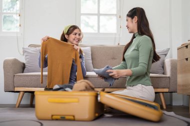 Asyalı kadın, arkadaşlarıyla seyahat için kıyafet paketlemeye hazırlanıyor. Asyalı güzel iki bayan arkadaşı tatil gezisi için çantanıza bir şeyler koymuş..