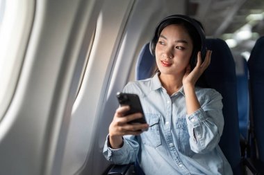 Birinci sınıf kabinde uçan genç bayan dinleme şarkısı, akıllı telefon kullanan kadın, akıllı telefondan müzik dinleyerek eğleniyor..