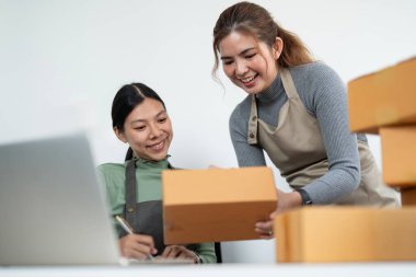Küçük işletme KOBİ sahibi, iki genç Asyalı iş sahibi kadın paket kutusu hazırlıyor ve çevrimiçi ürün siparişlerini müşteri, ambalaj, Alışveriş Online konseptine göndermek için kontrol ediyor.