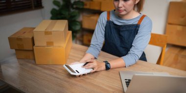 Kapalı görüşlü Asyalı kadın, onlara göndermeden önce bir müşteri listesi yazıyor. Web sitelerinde ve sosyal medyada ekomünikasyon işi yürütüyor..