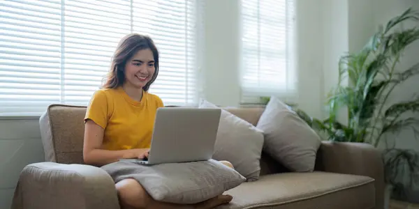 Young woman Asian using laptop pc computer on couch relax surfing the internet at home. lifestyle relaxation concept.