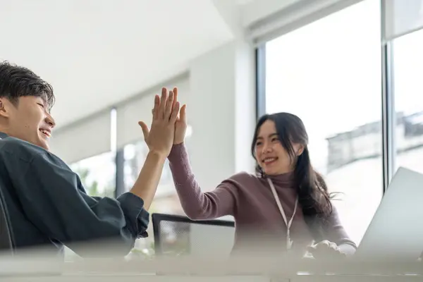 Successful business people giving each other a high five in a meeting. Two young business celebrating teamwork in an office.