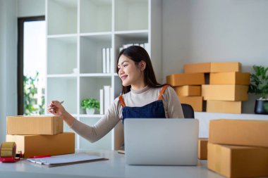 İnternetten ecommerce alışverişinde çalışan genç bir kadın. Genç bir kadın müşteriye teslim etmek için bir paket ürün satar. Çevrimiçi satış, ekommerce. Ürün çevrimiçi satılıyor.