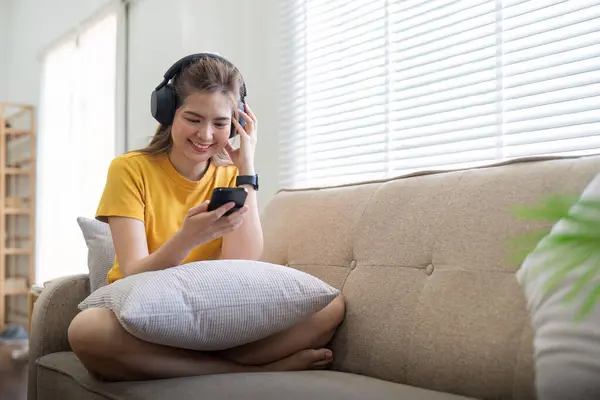 Genç Asyalı bir kadın müzik dinlemek ya da evde sohbet etmek için cep telefonu ve kulaklık kullanıyor..