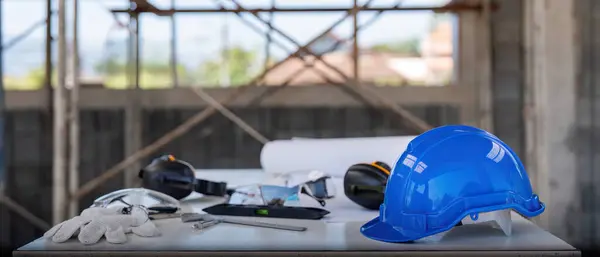 Engineer tool architecture blueprint design and safety helmet hardhat on meeting table with contractors paper project with engineer and architect working and discussing in background.