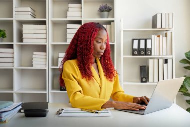 Pozitif Afrikalı iş kadını masanın başında oturuyor, dizüstü bilgisayarda yazıyor..