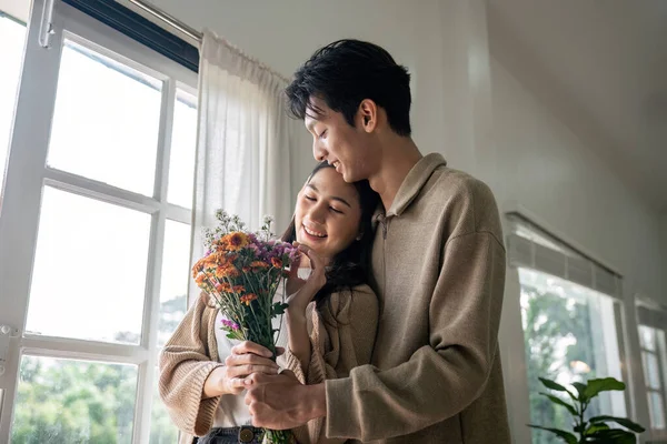 Romantický Mladý Asijský Pár Objímající Držení Květin Usmívající Obývacím Pokoji — Stock fotografie