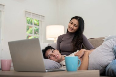 Mutlu çift Asyalı. Oturma odasında kanepede oturup dizüstü bilgisayarda birlikte video izliyorlar..