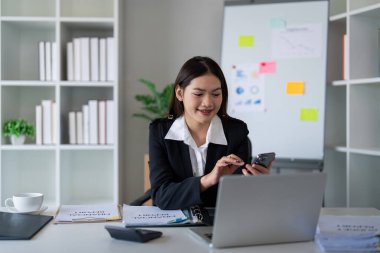 Ofiste bilgisayarını ve telefonunu kullanan genç ve güzel bir iş kadını..