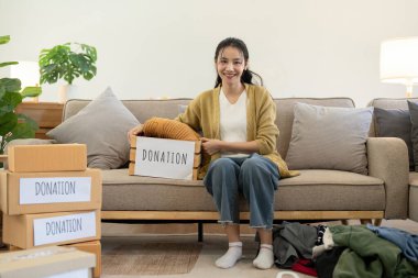 Asyalı bir kadın bağış kutusunu kıyafetlerle ve seçilmiş kıyafetlerle doldurmuş. Bağış ve kıyafet geri dönüşümü kavramı. Fakir insanlara yardım etmek.