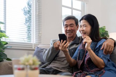 Akıllı telefon kullanan mutlu Asyalı çift evdeki internet sitesinde ekommerce alışverişi yapıyor..