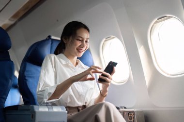 Seyahat ve teknoloji. Birinci sınıfta uçmak. Uçakta otururken akıllı telefon kullanan genç bir iş kadını..
