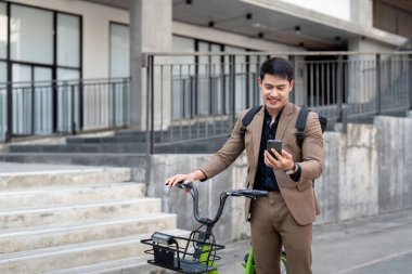 Takım elbiseli Asyalı işadamı işe gitmek için sabah işe giderken bisiklet sürüyor. Çevre taşımacılığı kavramı, sürdürülebilir yaşam tarzı kavramı.