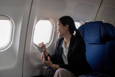Başarılı Asyalı iş kadını uçak kabininde oturuyor ve her yerden çalışıyor. Birinci sınıfta uçmak..