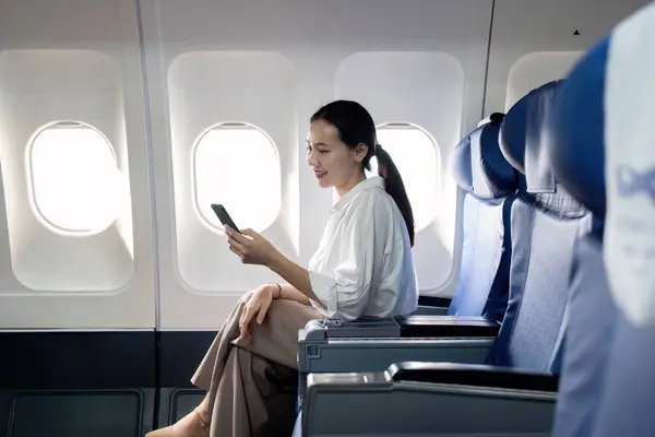 Woman Sitting Airplane Looking Her Phone She Smiling She Enjoying — Stock Photo, Image