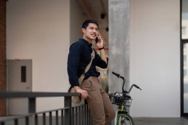 Çevre dostu, mutlu Asyalı genç iş adamı bisikleti ile şehir caddesindeki iş yerine sabah bisikletle gider..