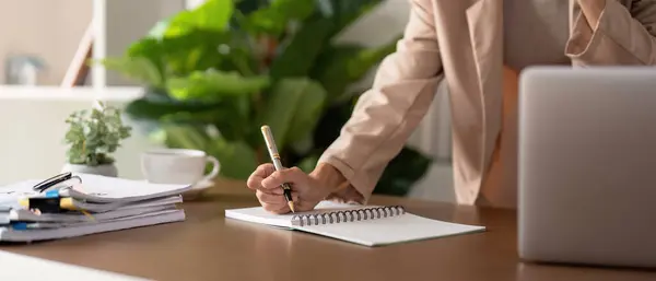 若いビジネスマンのペンが付いている手のクローズアップはノートを取っている間ノートパソコンが付いているテーブルで座っています 情報を分析します — ストック写真