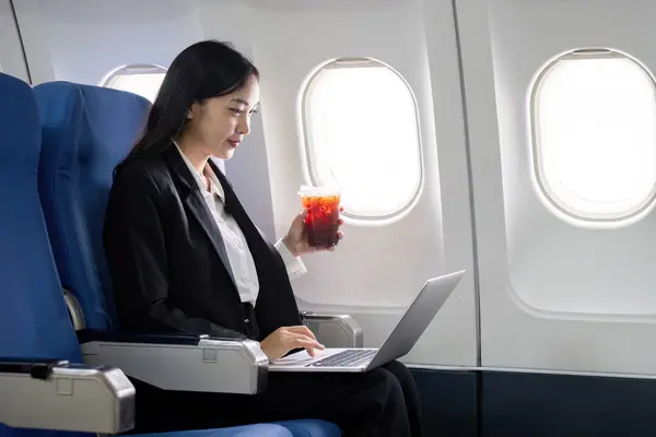 Asian young woman using laptop while drinking coffee at first class on airplane during flight, Traveling and Business concept.