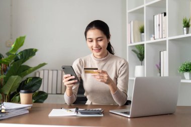Cep telefonuyla kredi kartı tutan mutlu genç Asyalı kadın. Gülümseyen kadın müşteri alışverişi akıllı telefondan para geri alma kavramını satın alıyor.