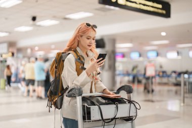 Havaalanında yürüyen Asyalı bir kadın. Cep telefonu, bavul ve genç bir bayanla birlikte iş ya da seyahat için uluslararası bir seyahate çıkmak..