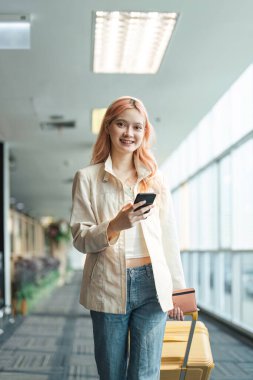 Havaalanında gezgin kadın Asyalı ve tatil için bavul, gülümse ve telefon kontrol biletini tut. Bavullu, yurtdışında ve pasaportlu ve seyahatli bir bayan yolcu..