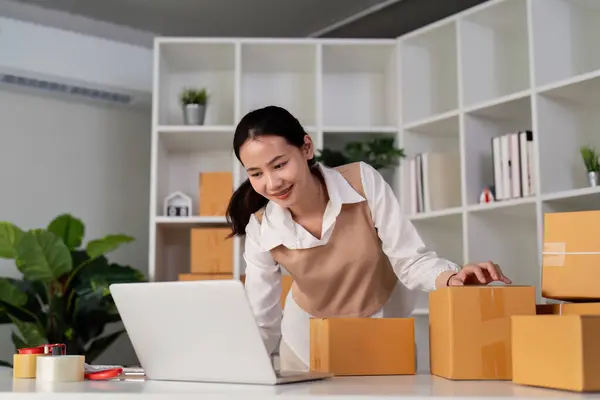 stock image Young woman working online ecommerce shopping at her shop. Young woman seller prepare parcel box of product for deliver to customer. Online selling, ecommerce. Selling products online.