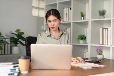 Asyalı iş kadını finansal bütçe raporunu analiz etmek ve ofis masasında gelecek planlamak için dizüstü bilgisayar kullanıyor..