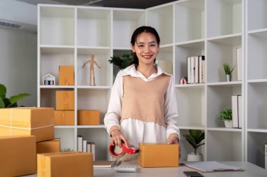 Asyalı kadın, paketleme, nakliye, çevrimiçi satış İnternet pazarlama ekommerce konsepti başlangıç iş fikri için paket kutuları eklemek için koli bandı kullanıyor.