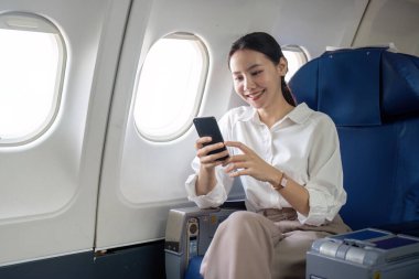 Seyahat ve teknoloji. Birinci sınıfta uçmak. Uçakta otururken akıllı telefon kullanan genç bir iş kadını..