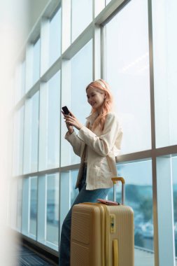 Havaalanında gezgin kadın Asyalı ve tatil için bavul, gülümse ve telefon kontrol biletinin üzerinde konuş. Bavullu, yurtdışında ve pasaportlu ve seyahatli bir bayan yolcu..