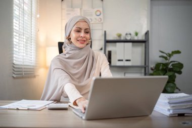 Başörtüsü takmış Asyalı Müslüman iş kadını modern ofiste kağıt belgelerle çalışıyor. çeşitlilik ve ofis kavramı.