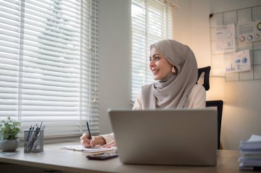 Başörtüsü takmış Asyalı Müslüman iş kadını modern ofiste kağıt belgelerle çalışıyor. çeşitlilik ve ofis kavramı.