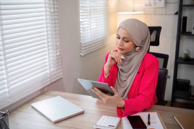 Genç Müslüman iş kadını tesettür modern ofiste dijital tablet kullanmaktan mutlu.