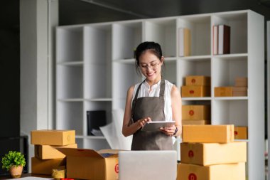 İnternetten ecommerce alışverişinde çalışan genç bir kadın. Genç bir kadın müşteriye teslim etmek için bir paket ürün satar. Çevrimiçi satış, ekommerce. Ürün çevrimiçi satılıyor.