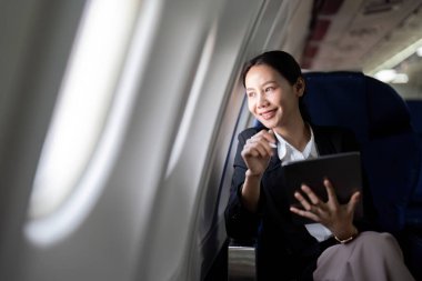 Başarılı Asyalı iş kadını uçak kabininde oturuyor ve her yerden çalışıyor. Birinci sınıfta uçmak..