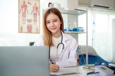 Sağlık kliniğindeki ya da hastanedeki ofis masasında dizüstü bilgisayarda çalışan kadın doktor.