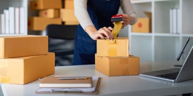 Kadınlar paketleme, nakliyat, çevrimiçi satış, internet pazarlama ekommerce konsepti girişimi fikrine ürün hazırlamak için koli bandı kullanırlar..