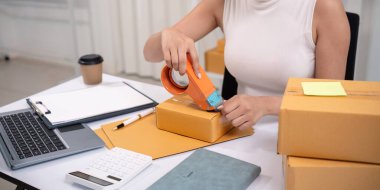 Asyalı kadın, paketleme, nakliye, çevrimiçi satış İnternet pazarlama ekommerce konsepti başlangıç iş fikri için paket kutuları eklemek için koli bandı kullanıyor.