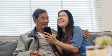 Akıllı telefon kullanan mutlu Asyalı çift evdeki internet sitesinde ekommerce alışverişi yapıyor..